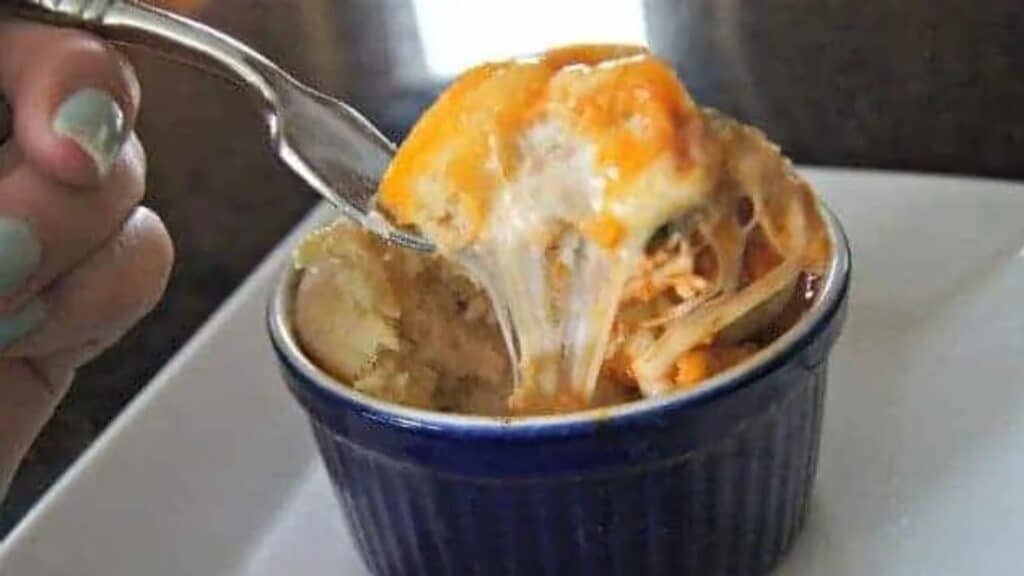 Image shows a fork with a great cheese pull taking a bite from a blue ramekin containing a chicken pizza pot pie.