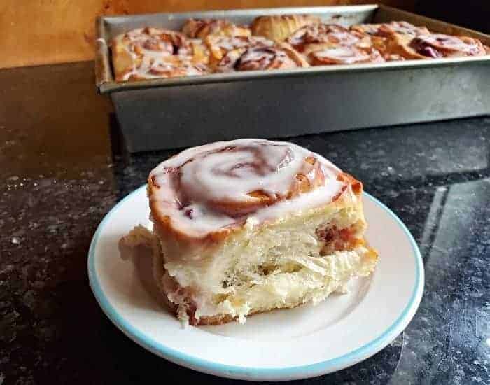 Image shows a cherry cinnamon roll on a small plate with the full pan behind it.