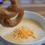 Image shows Pretzel dipping into beer cheese soup.