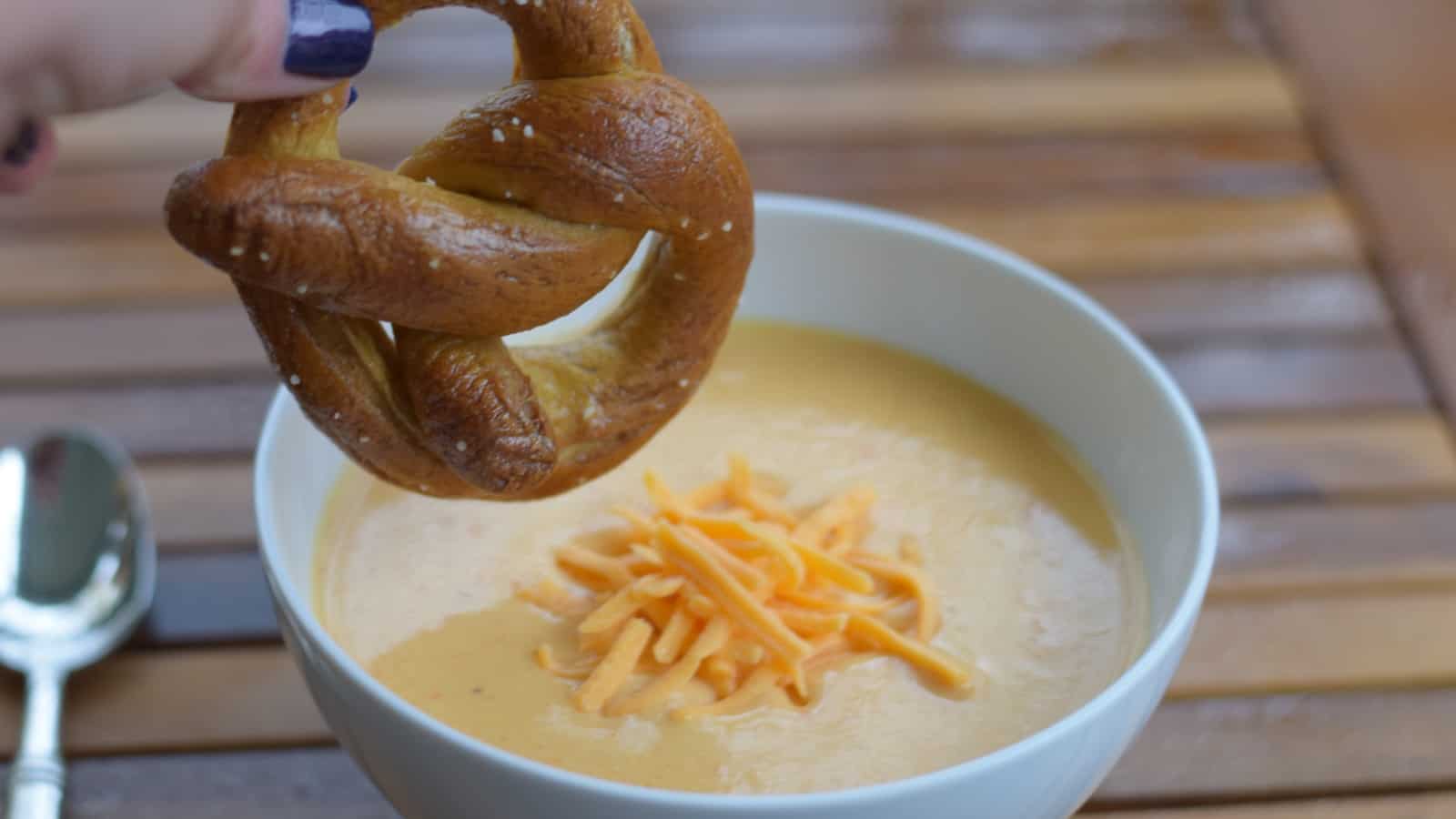 Image shows Pretzel dipping into beer cheese soup.