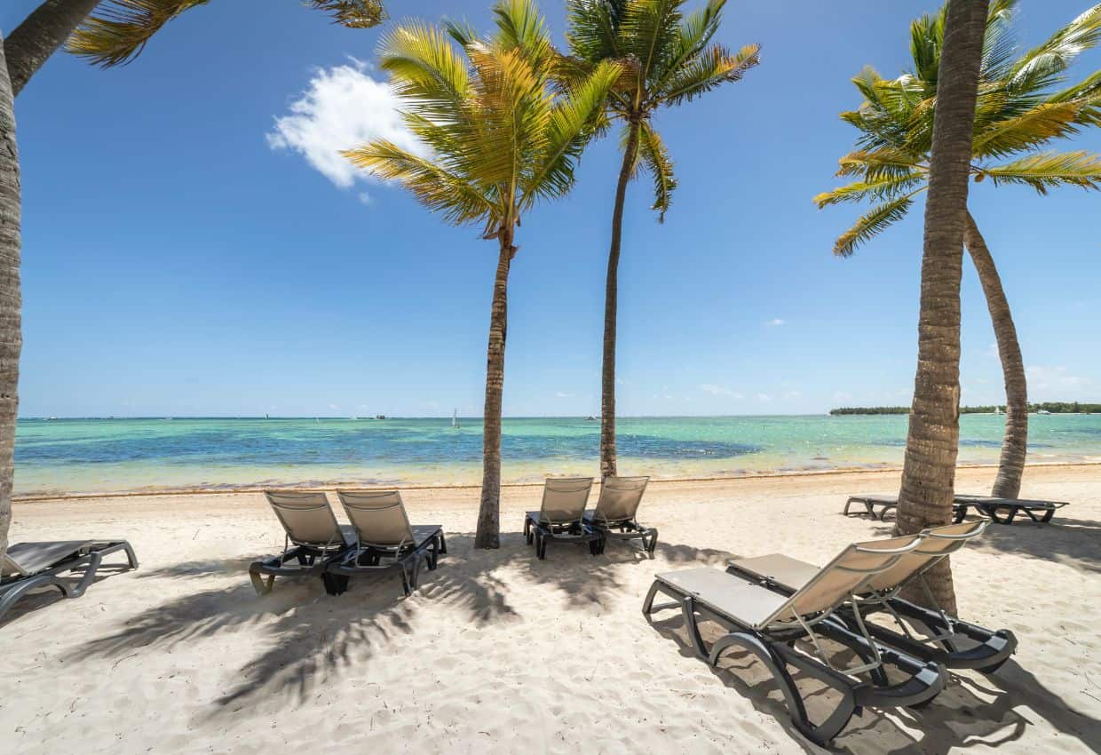 Image shows Punta Cana beach with chairs and palm trees.