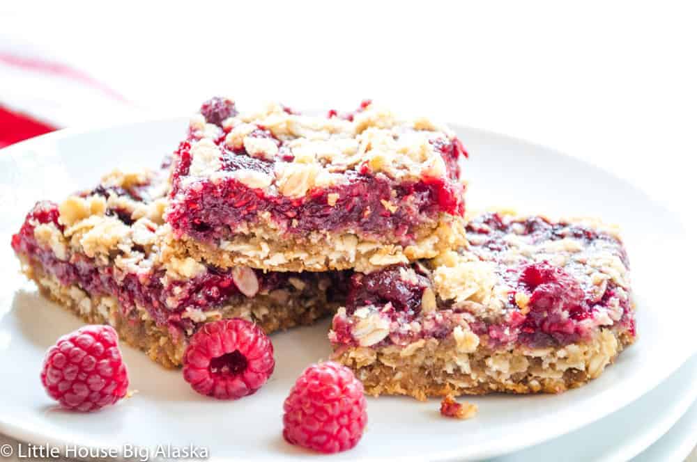 A stack of raspberry cookie bars with fresh raspberries on the plate too.