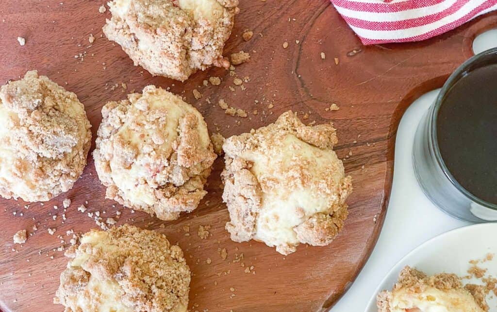 Rhubarb muffins with streusel on a round cutting board and a cup of coffee.