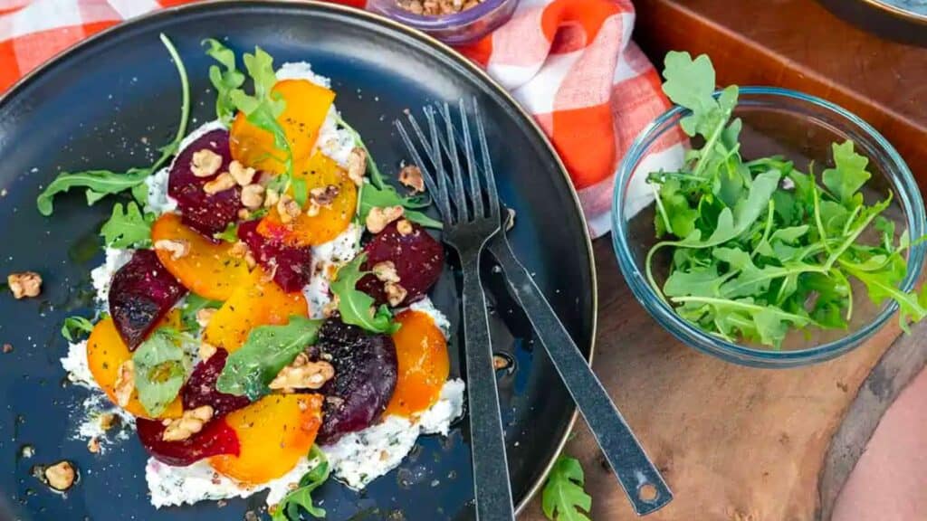 Plate of roasted beets with greens on goat cheese spread.