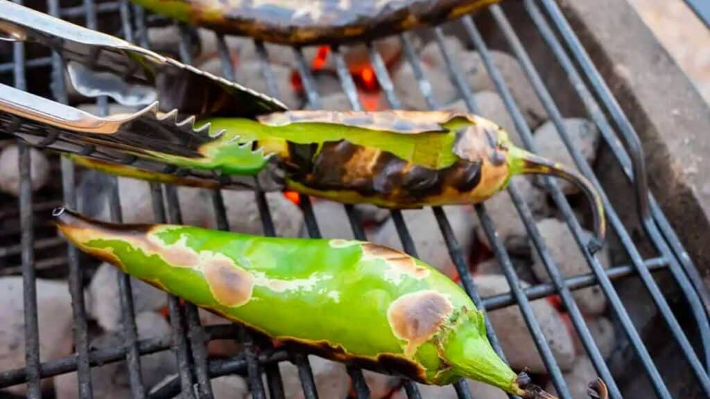 Tongs flipping hatch chiles on grill.