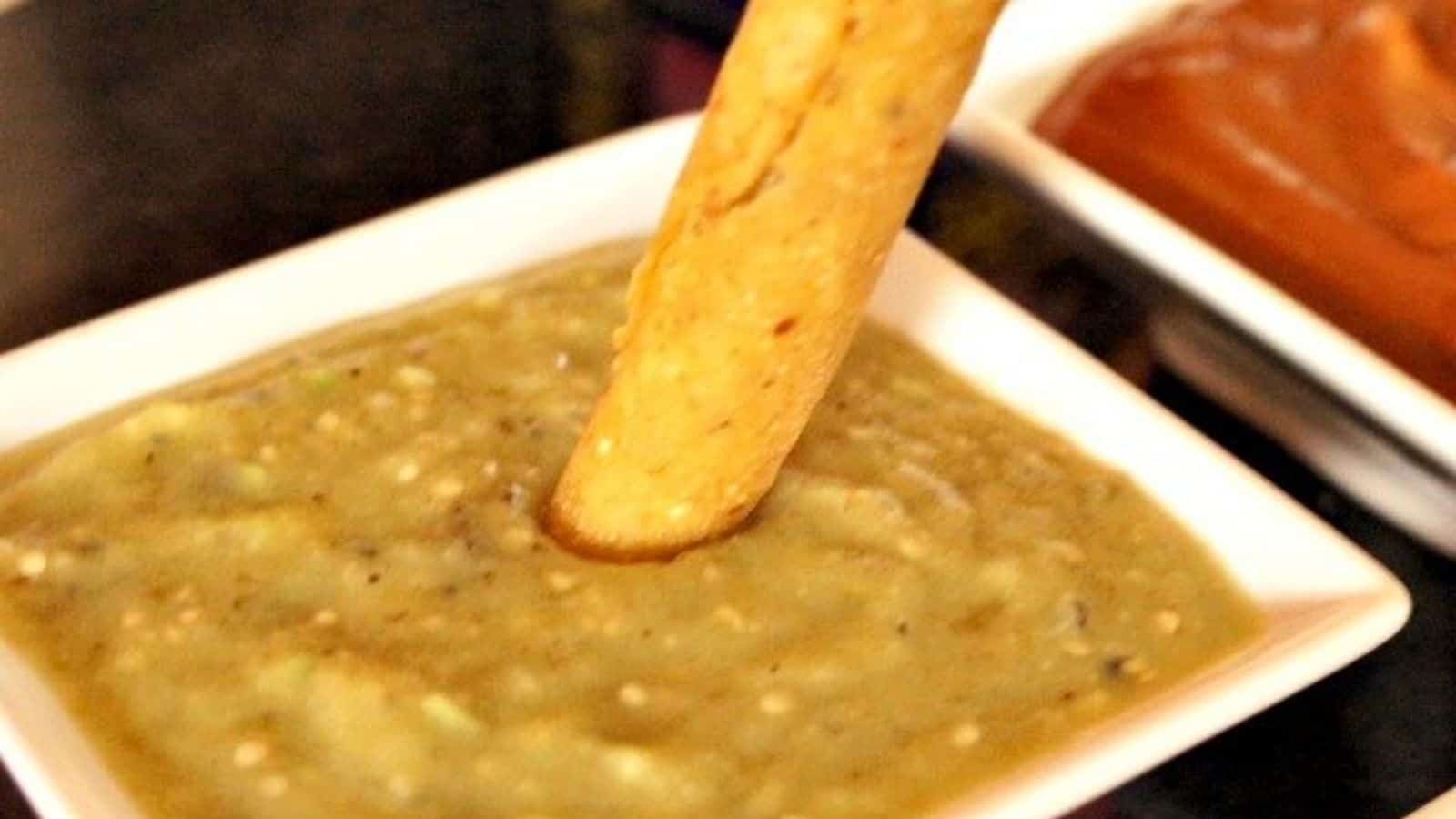 Image shows a taquito dipping into a white bowl of Roasted Tomatillo Salsa.