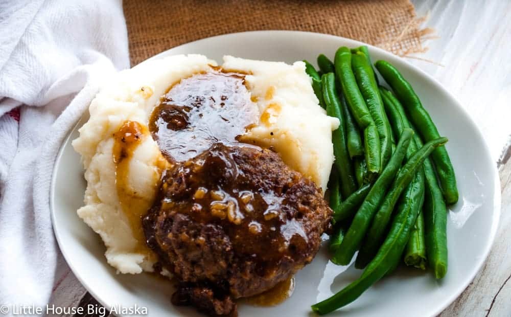 Salisbury steak on a plate with green beans and mashed potatoes.