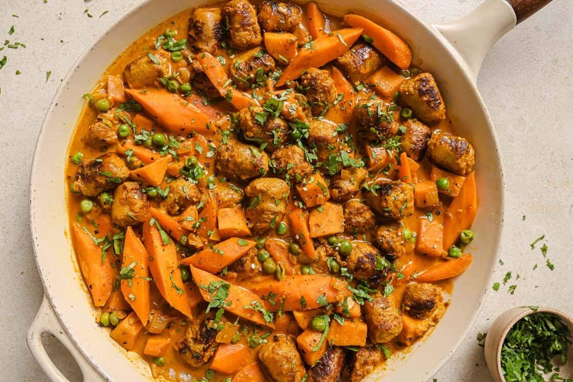 Sausage curry in a skillet garnished with herbs.