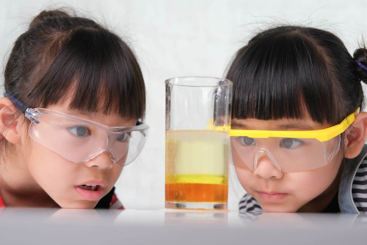 Two girls with safety goggles looking at liquid in beaker.