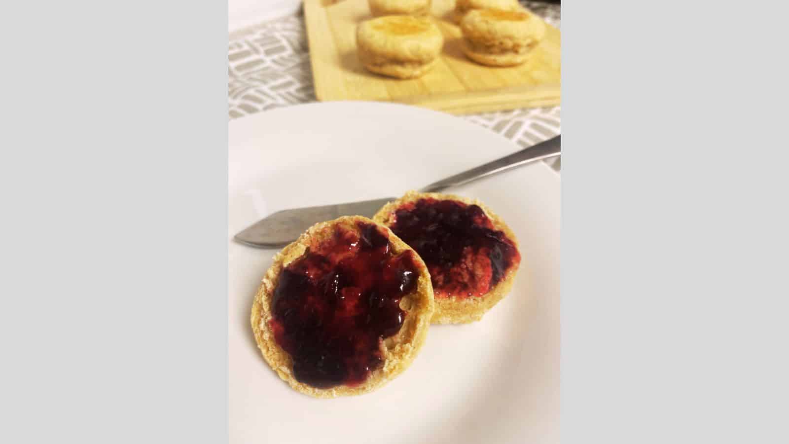 Round scones with jam on white plate.
