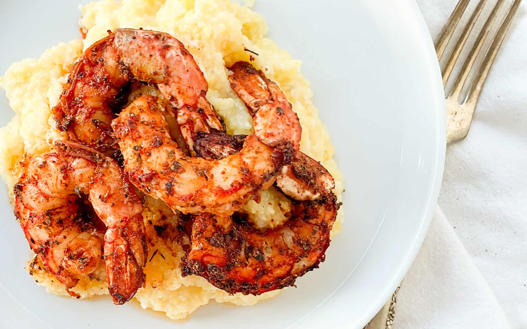 Blackened shrimp on grits with a fork on the right side.