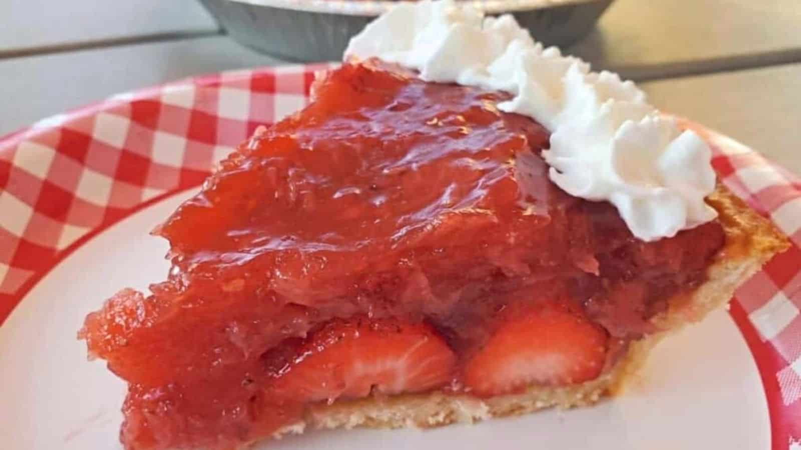 Slice of strawberry pie on a plate with the whole pie in the background.