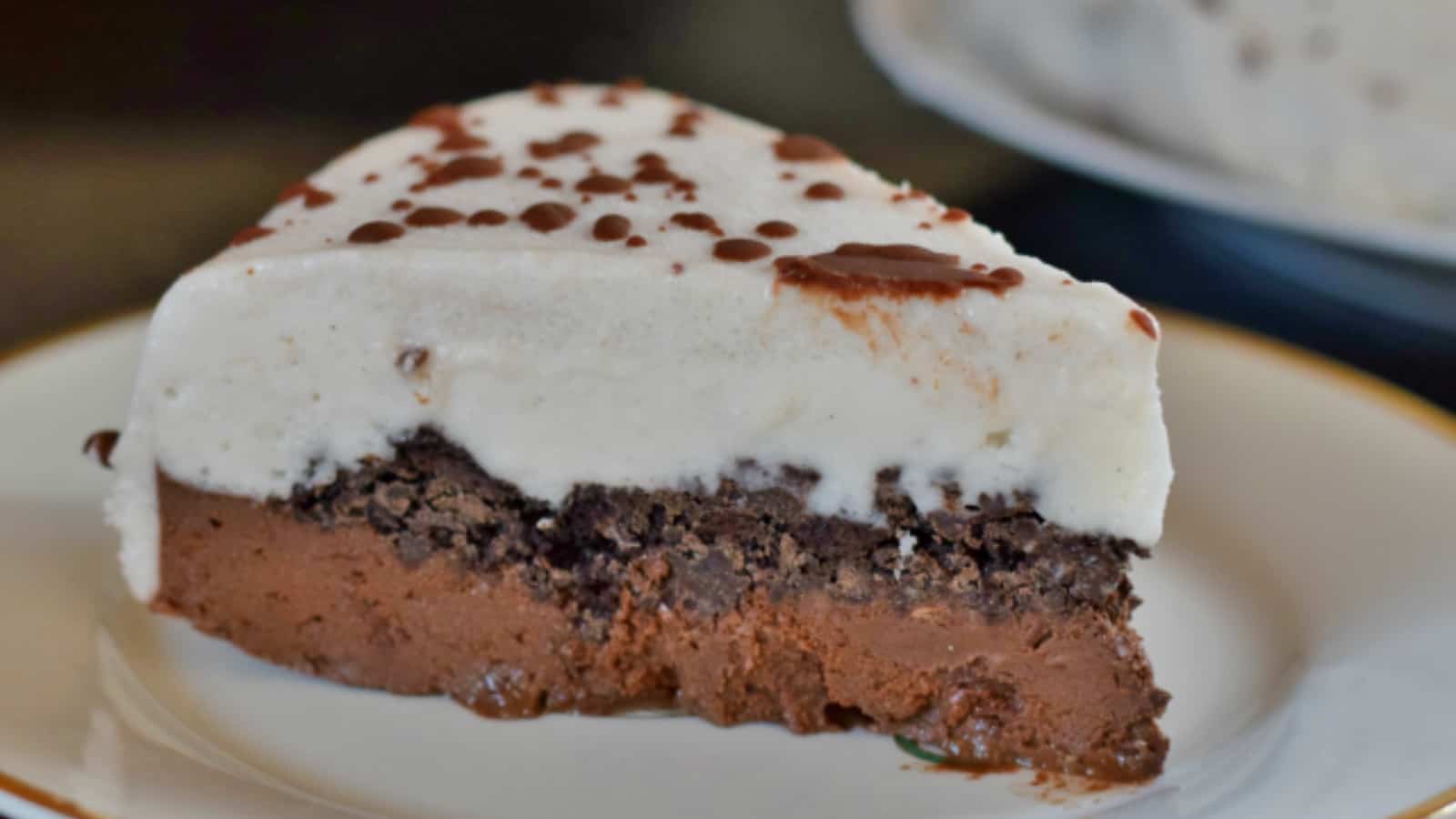 Image shows a slice of an ice cream cake with the full cake in the background to the side.