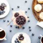 Small batch blueberry jam featured in the middle of the table with biscuits, coffee, and serving plates.