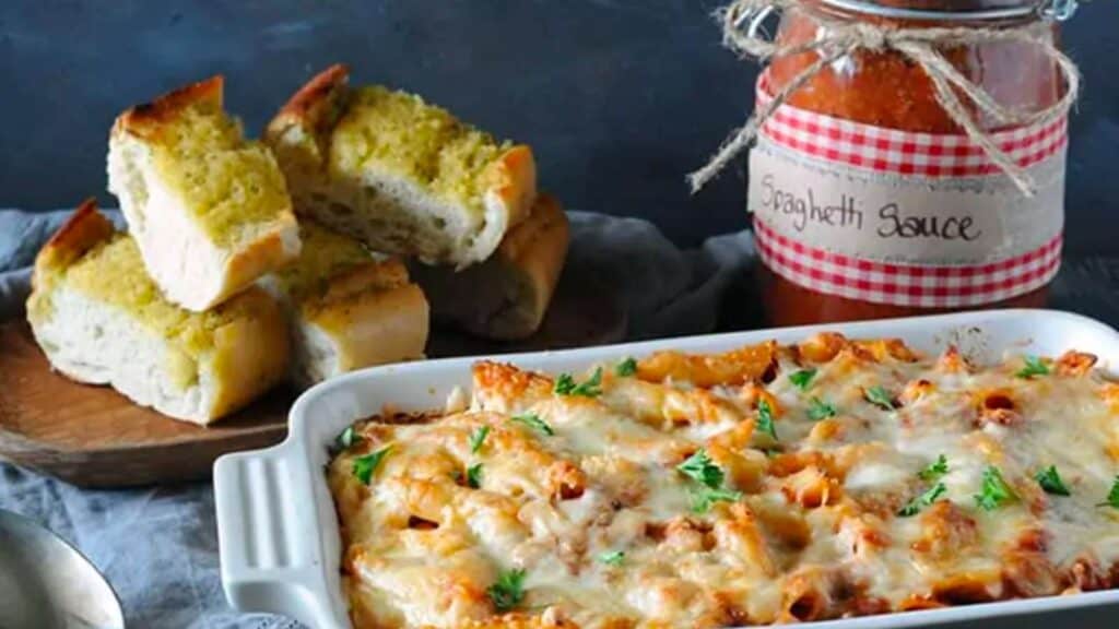 Jar of spaghetti sauce next to pasta dish and bread.