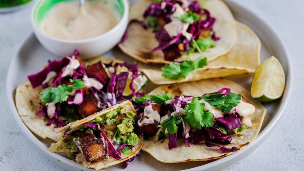 side view of tacos on a plate, one with bite taken out.