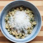 Image shows an overhead shot of Spinach Parmesan Quinoa in a blue bowl with a sprinkle of cheese on top.