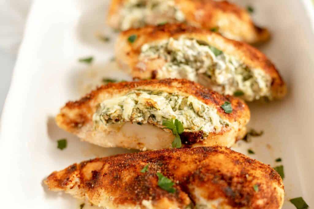 A line of stuffed chicken breasts on a white platter.