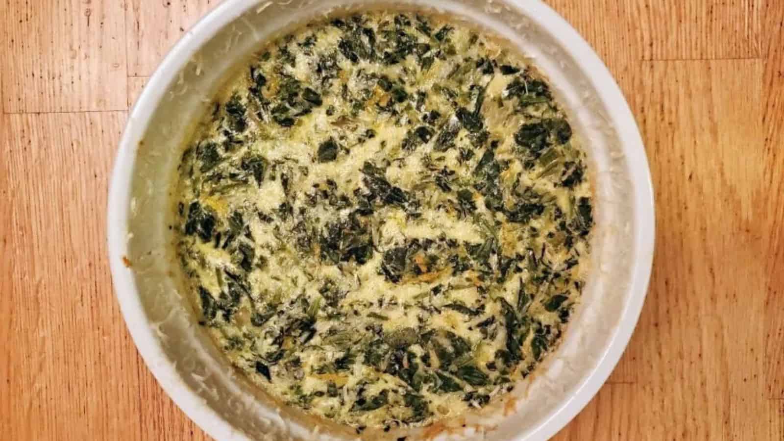 This photo shows and overhead shot of a spinach souffle in a round white casserole dish.