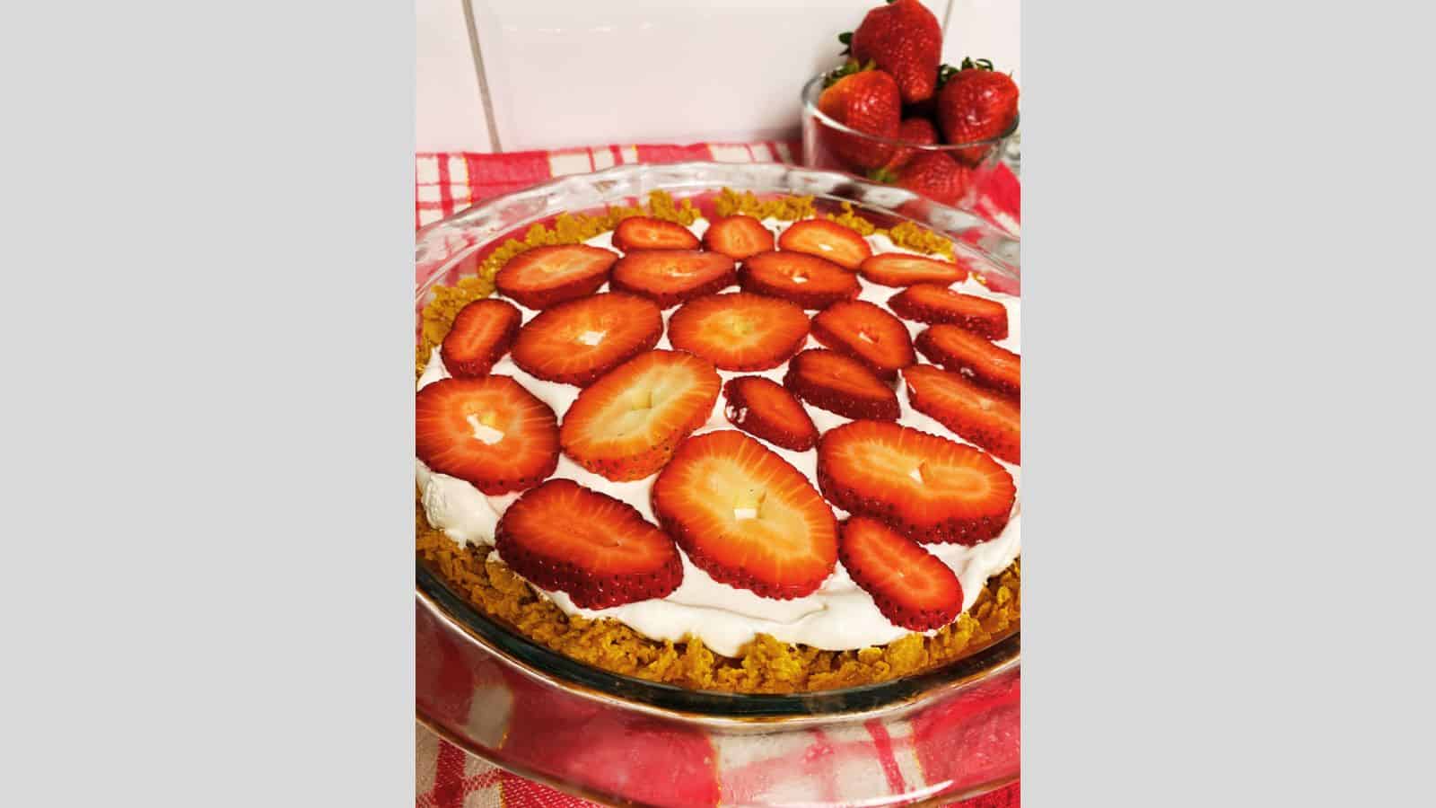 Strawberry cream pie in clear pie dish with bowl of strawberries in background.