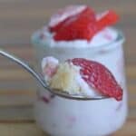 Image shows a spoon holding a bite of Strawberry Lemonade Icebox Cake with the full container behind it.