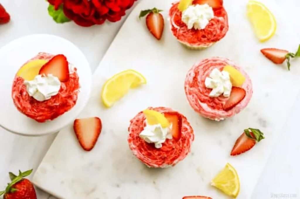 Overhead shot of mini cheesecakes and slices of lemon and strawberries.