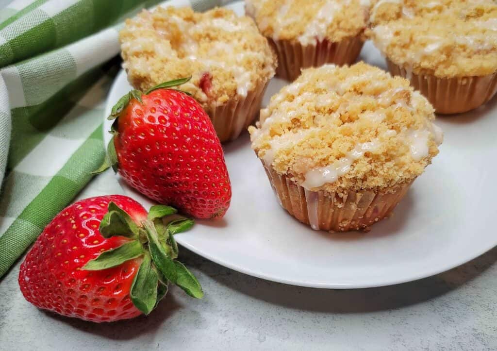 A plate of bakery style strawberry muffins with fresh strawberries.