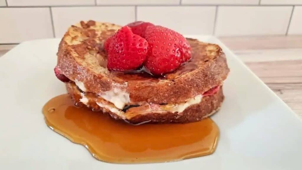 Image shows Strawberry Stuffed French Toast on a white plate with syrup around it.