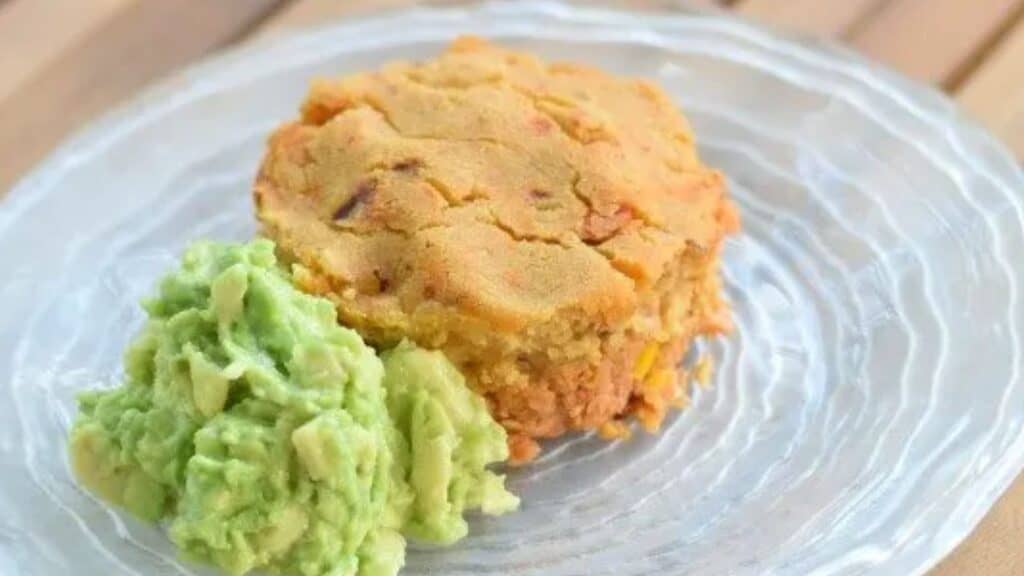 Image shows a Tamale pot pie on a glass plate with guacamole sitting next to it.