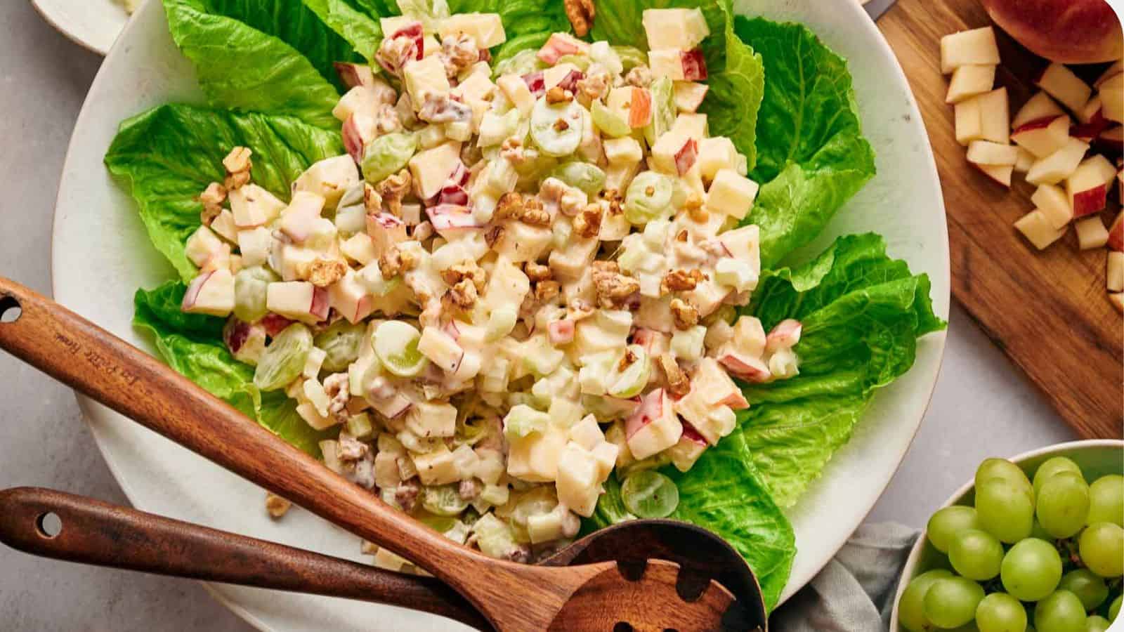 Waldorf salad on a bed of lettuce, with salad servers resting on top.