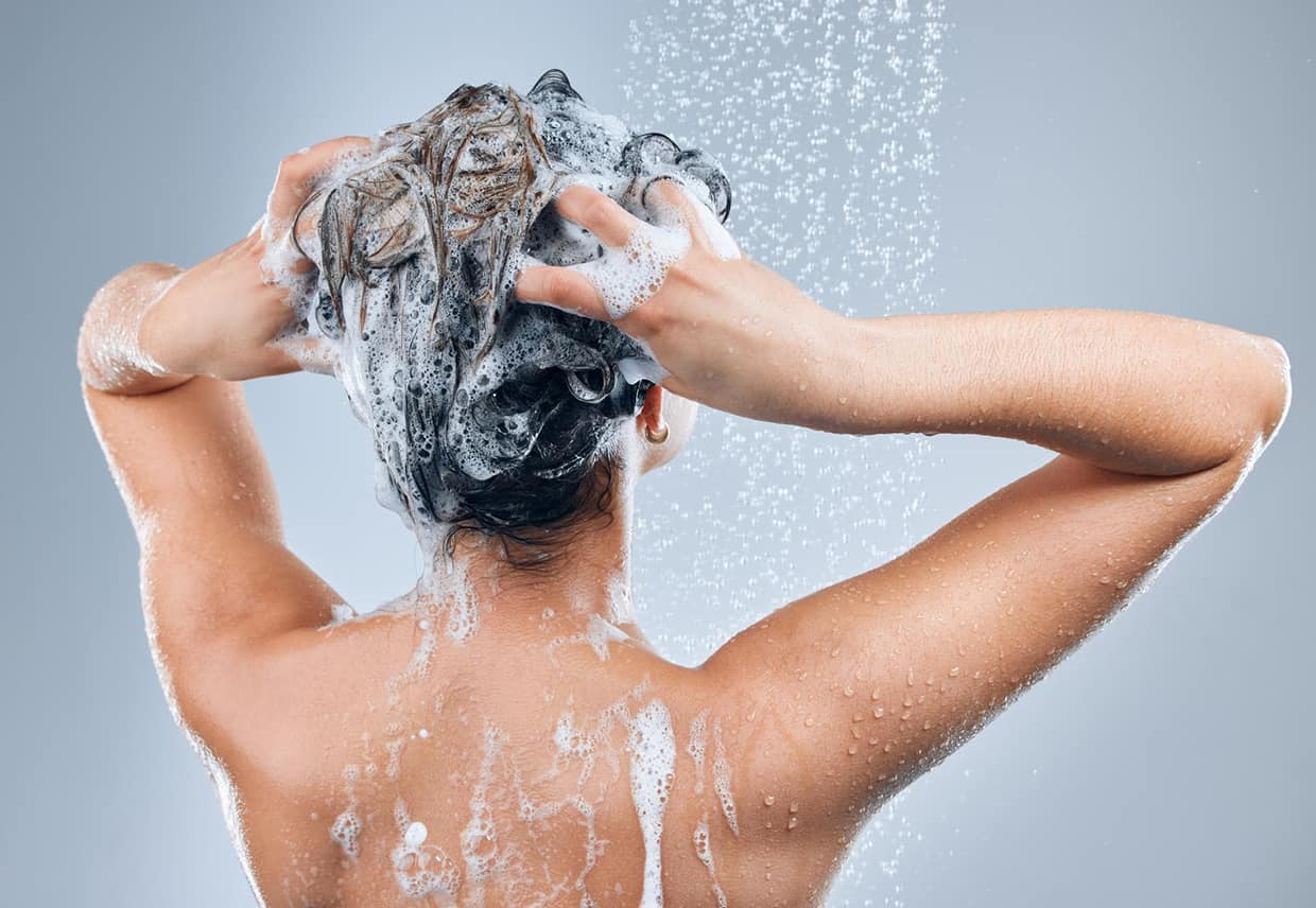 Create a great hair care routine. an unrecognizable woman washing her hair in the shower against a grey background.