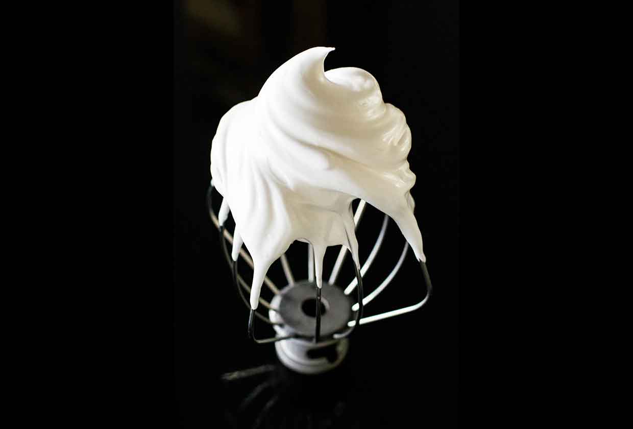 Whipped meringue on an upside down wire whisk from a stand mixer.
