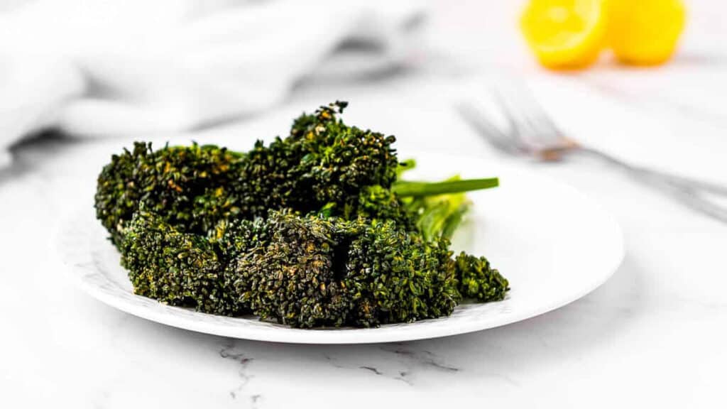 Air fried broccolini on a plate with lemons in the background.