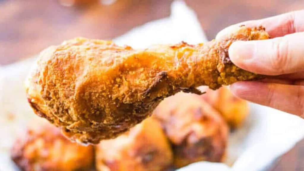 A hand holding a crispy piece of fried chicken made with an air fryer.