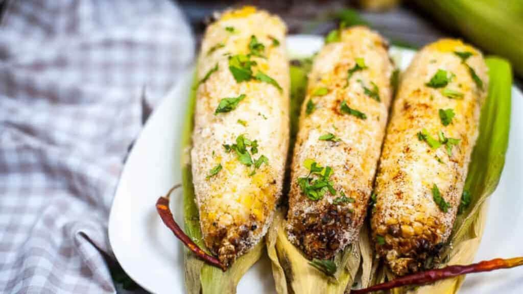 Air fryer elote on a white plate with a blue-and-white napkin.