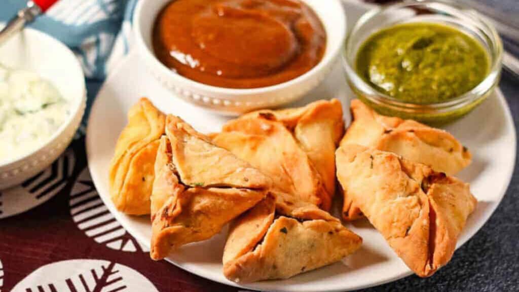 Air fryer samosas on a white plate with chutneys.