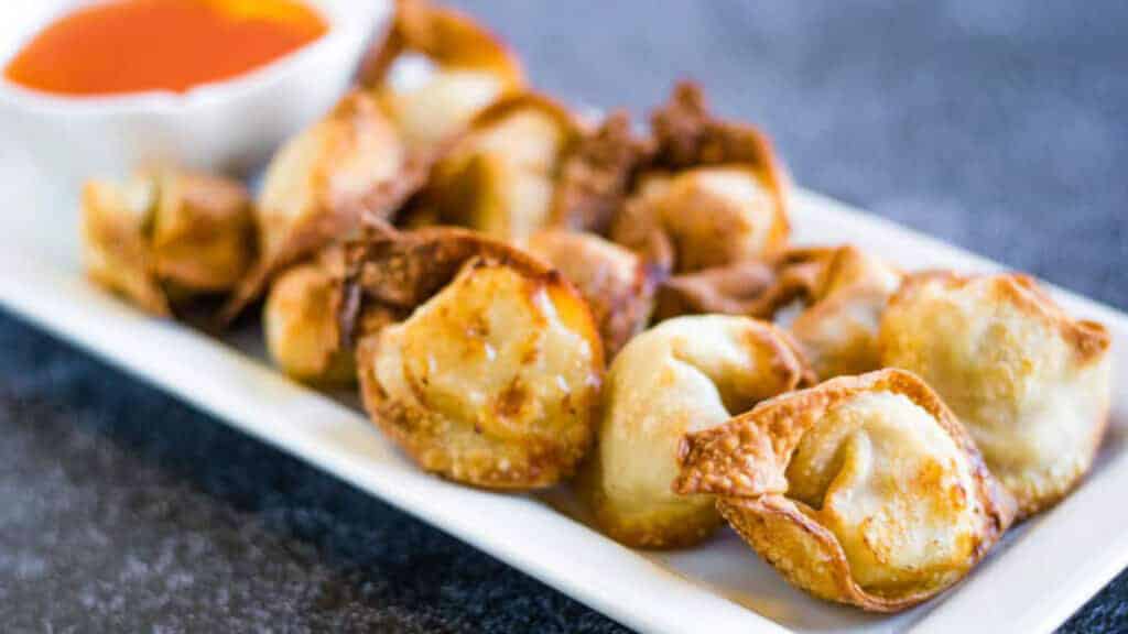 Air fryer wontons on a white plate with sweet chili dipping sauce.