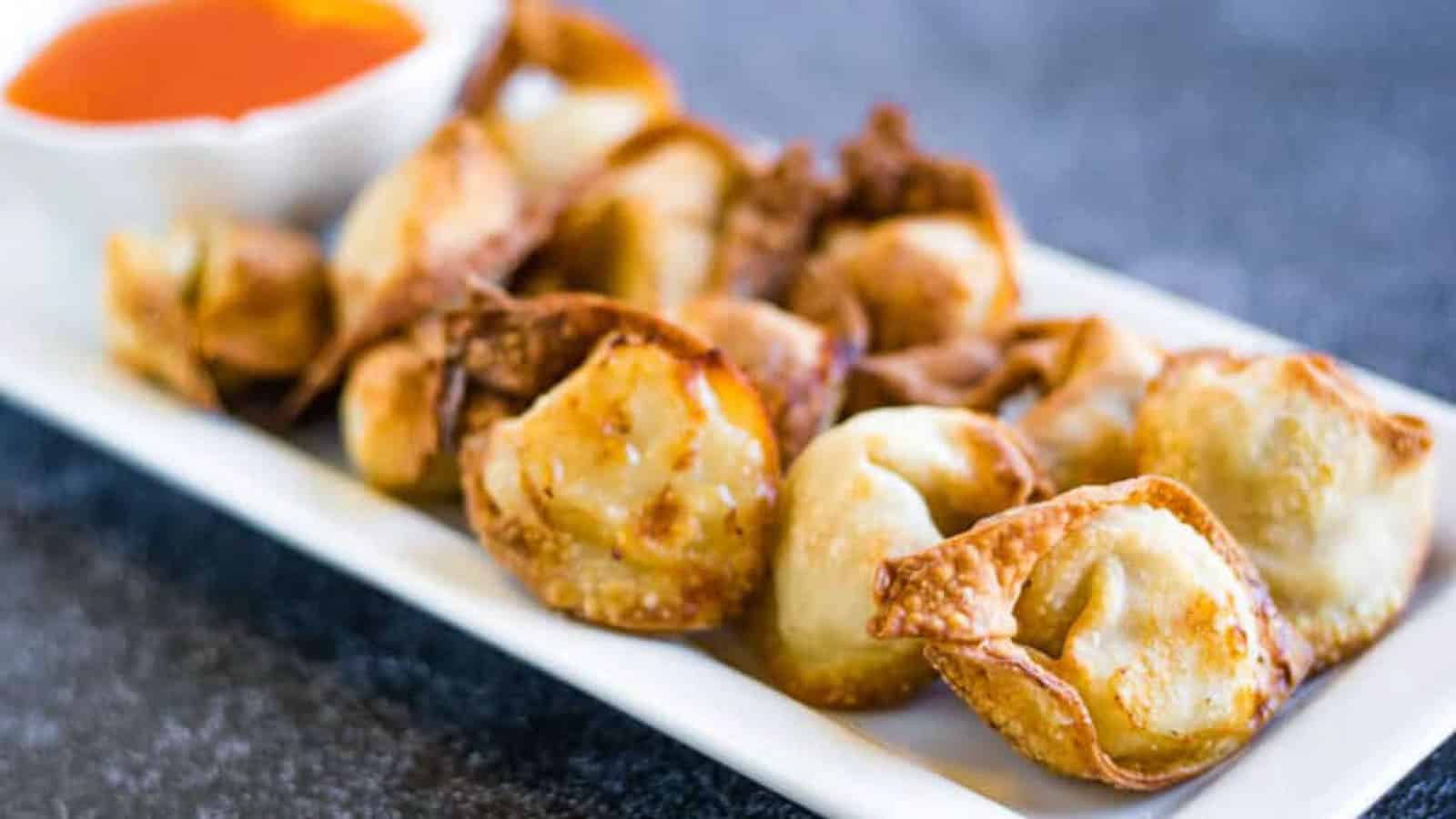 Air fryer wontons on a plate with dipping sauce.