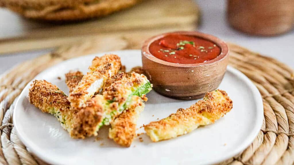 Air fryer zucchini fries on a white plate with a dipping bowl of ketchup.