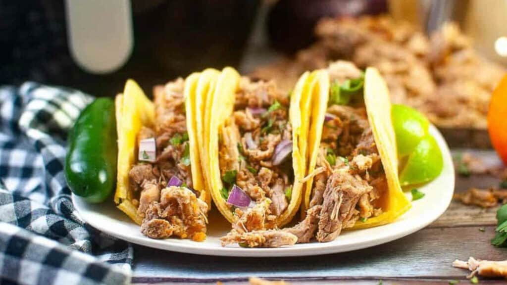 three tacos made from air fryer carnitas on a plate with onions, cilantro and lime.