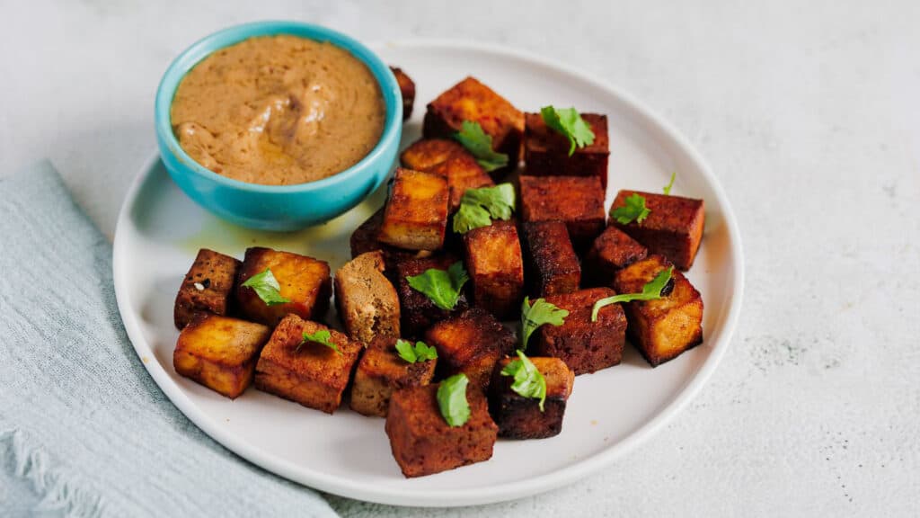 Fried tofu on a white plate with dipping sauce.