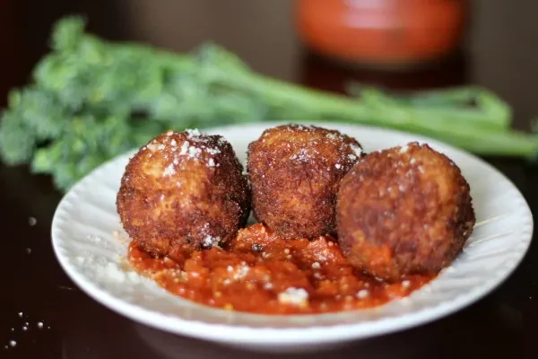 plate of arancini with marinara and broccolini blurred in background