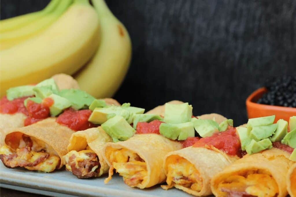 Plate of breakfast taquitos, topped with salsa and avocados.