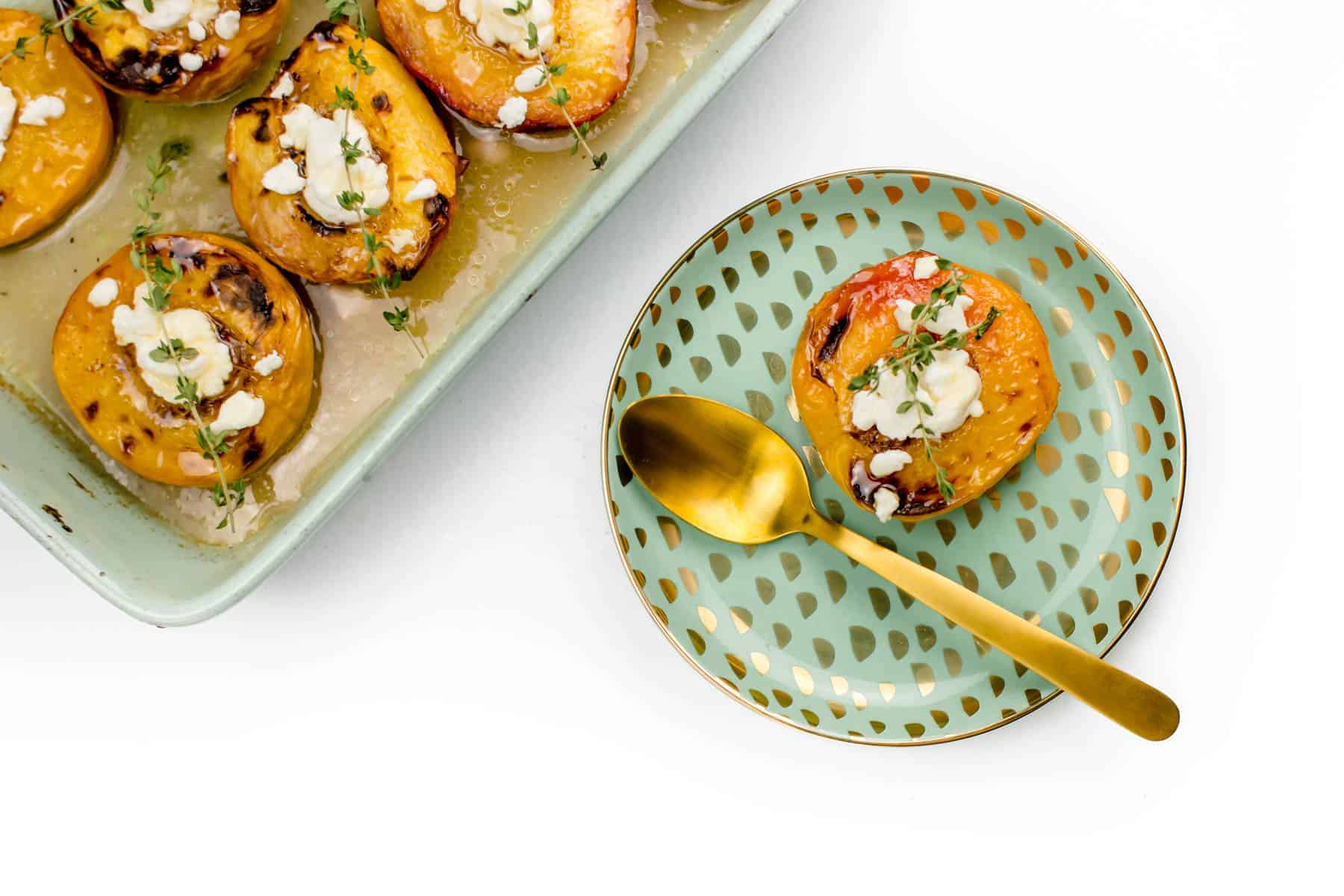 Baked peaches in a green baking dish next to a speckled plate with a baked peach on it.