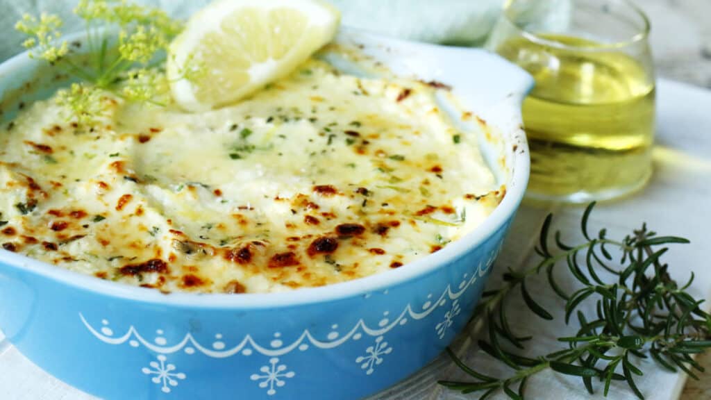 Baked ricotta dip in a blue bowl with herbs and lemon slice.