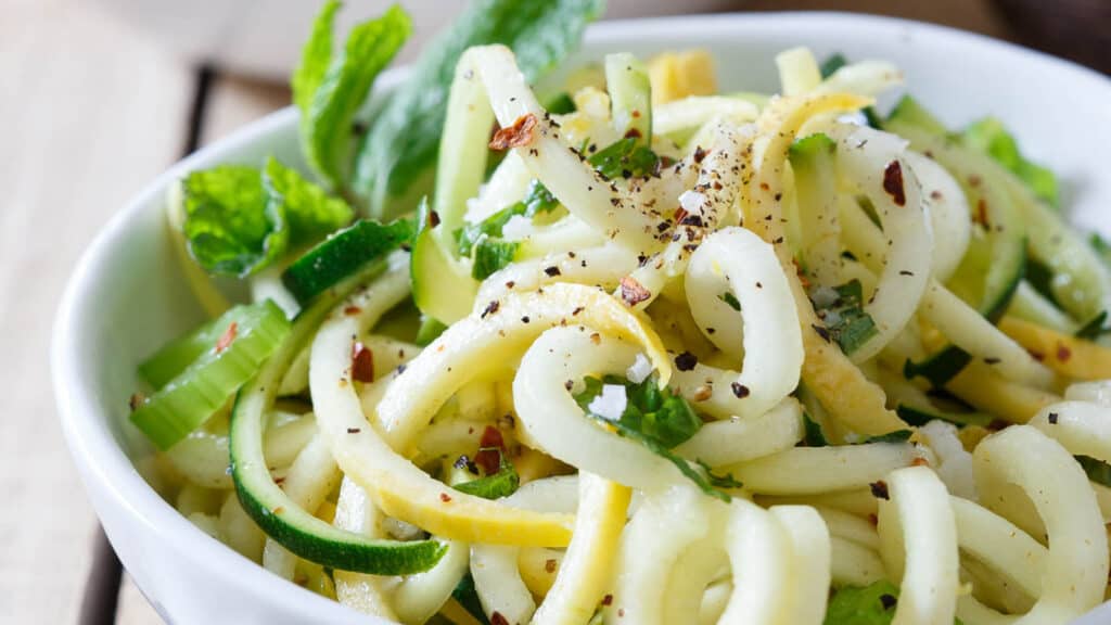 Basil mint squash noodles with freshly ground black pepper in a white bowl.