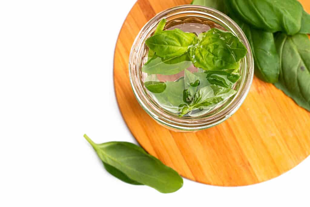 A jar of basil syrup and basil leaves on a wood cutting board. 