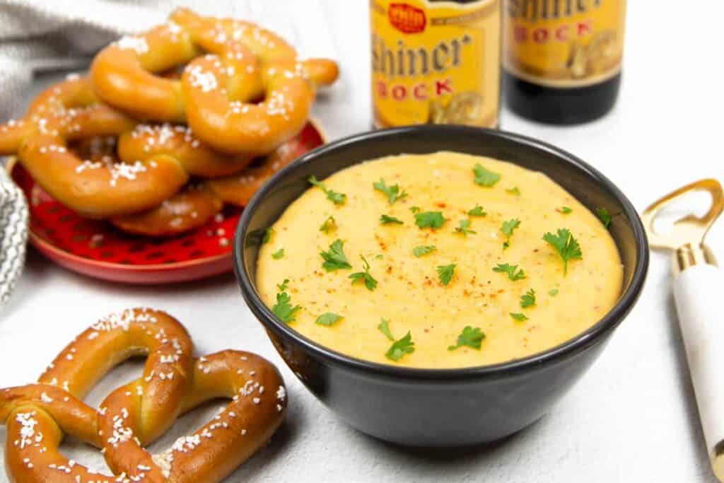 Soft pretzels next to a bowl of beer cheese dip and two beers in bottles.