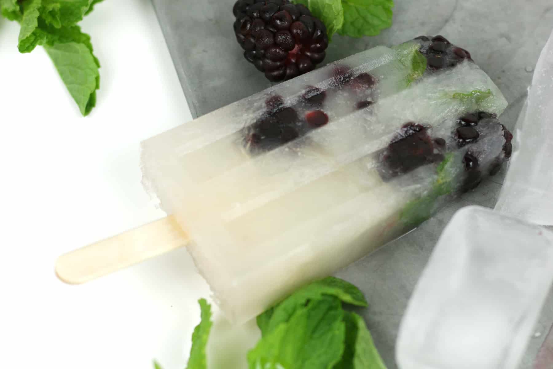 A Blackberry Mojito Popsicle on a silver tray with fresh blackberries and mint leaves.