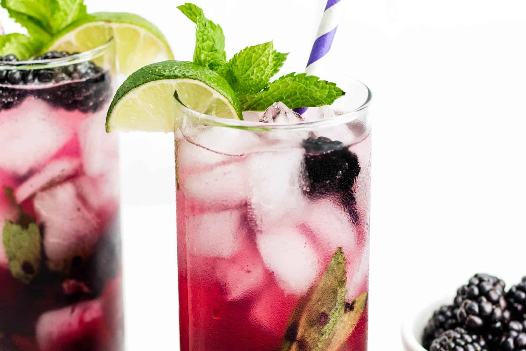 Two mojitos made with blackberries sit side by side next to a bowl of whole berries.